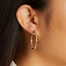Model. Close-up of an ear wearing a gold hoop earring with clear stones.