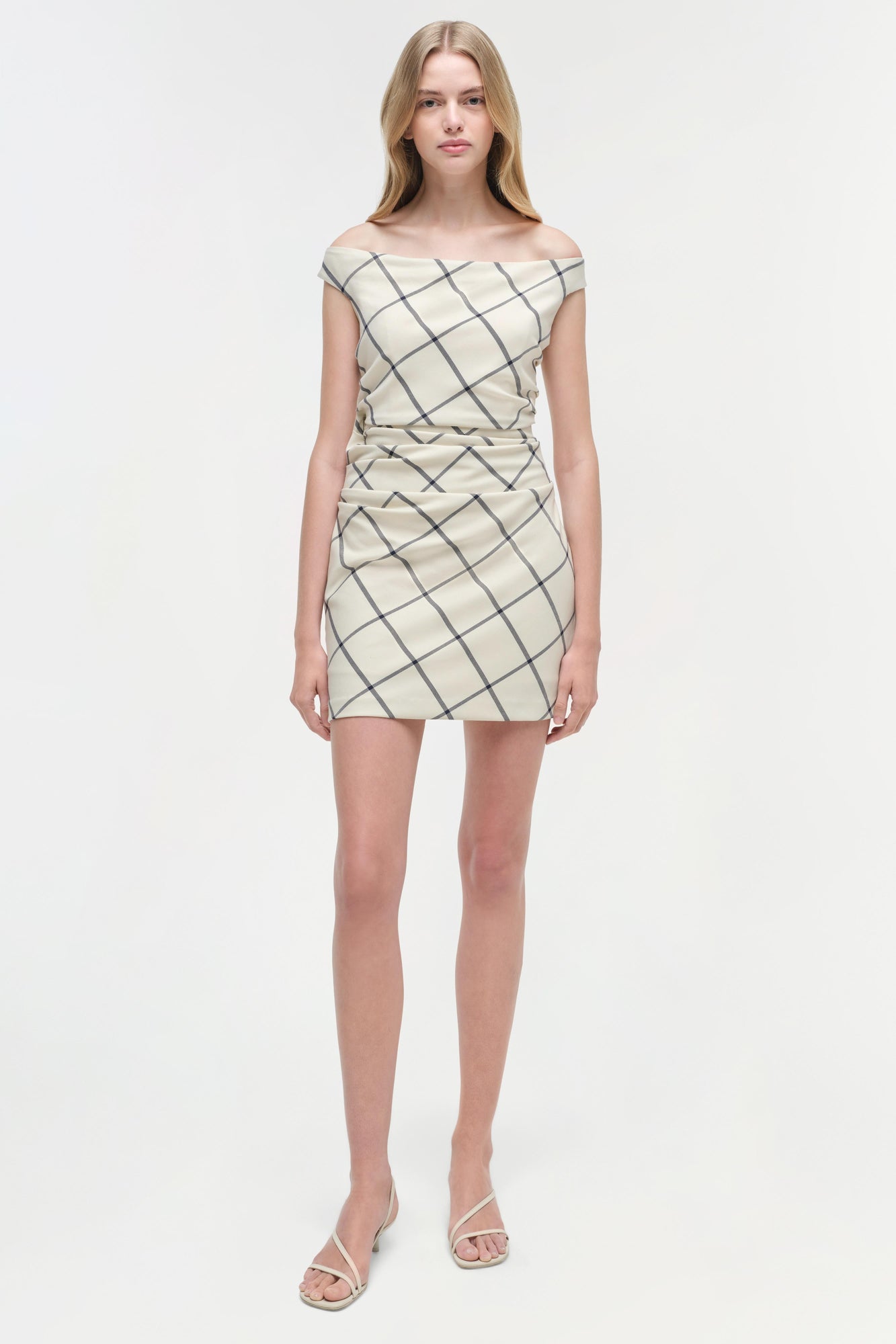 Cream mini dress with diagonal grid pattern and off-shoulder neckline, styled with white sandals.