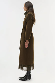 Olive-brown coat with fringe trim at shoulders and hem, belted waist, worn with black boots.