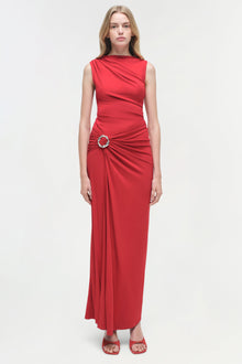 Woman wearing a sleeveless red jersey gown with ruched waist detail and metal ring accent.