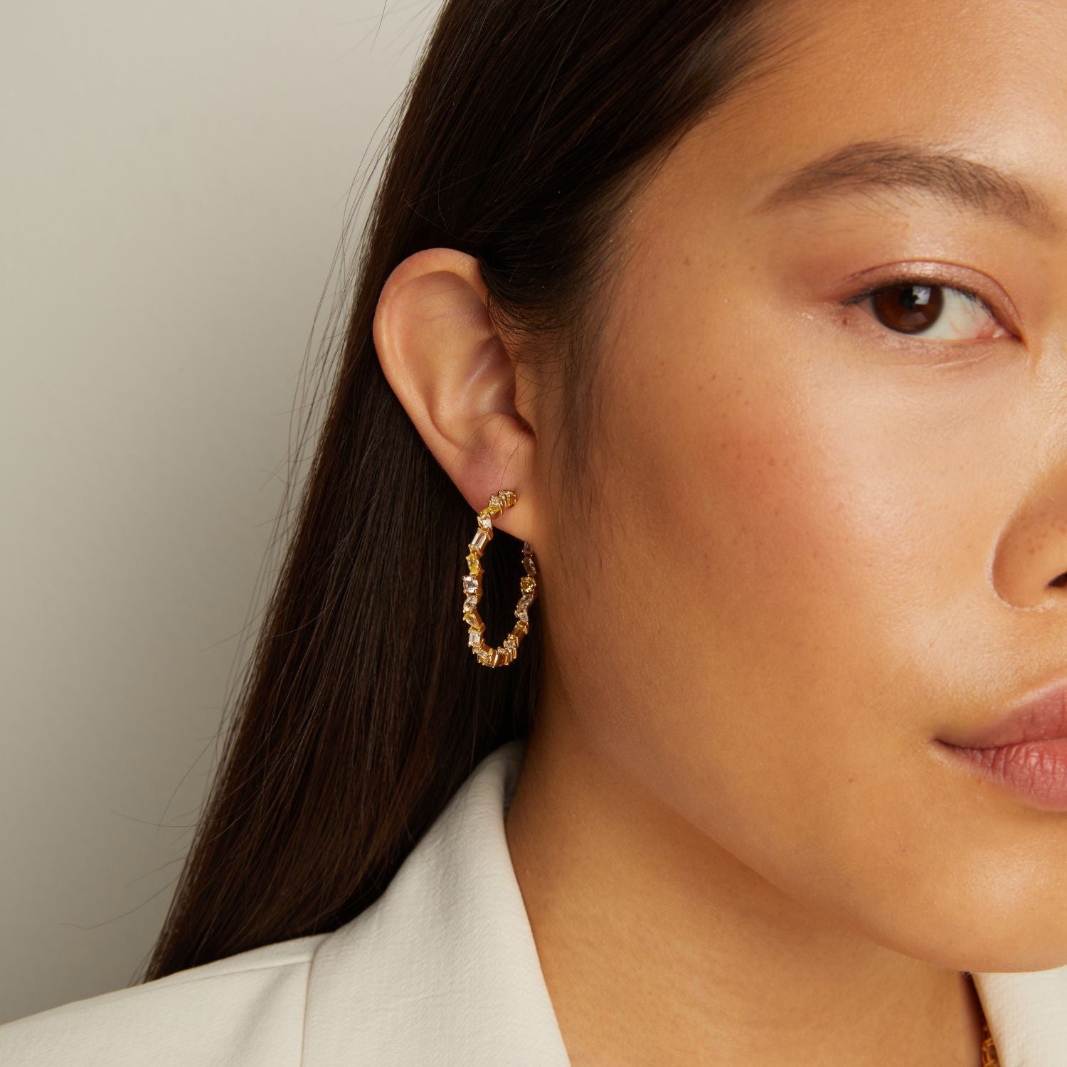 Model. Close-up of a woman wearing gold hoop earrings with a neutral background