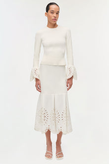Cream knit midi skirt with openwork embroidered hem and pleated waist detail, worn with matching long-sleeve top.