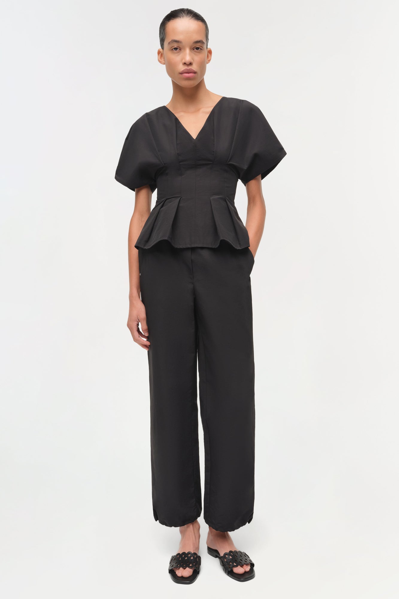 Black cotton faille pull-on pants with wide legs and scalloped hem, shown on model wearing matching peplum top.