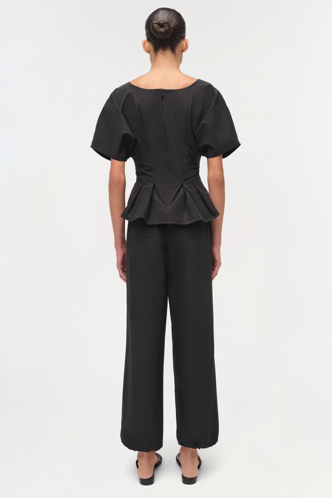 Black cotton top with short puffed sleeves and ruched peplum waist, shown from back view.