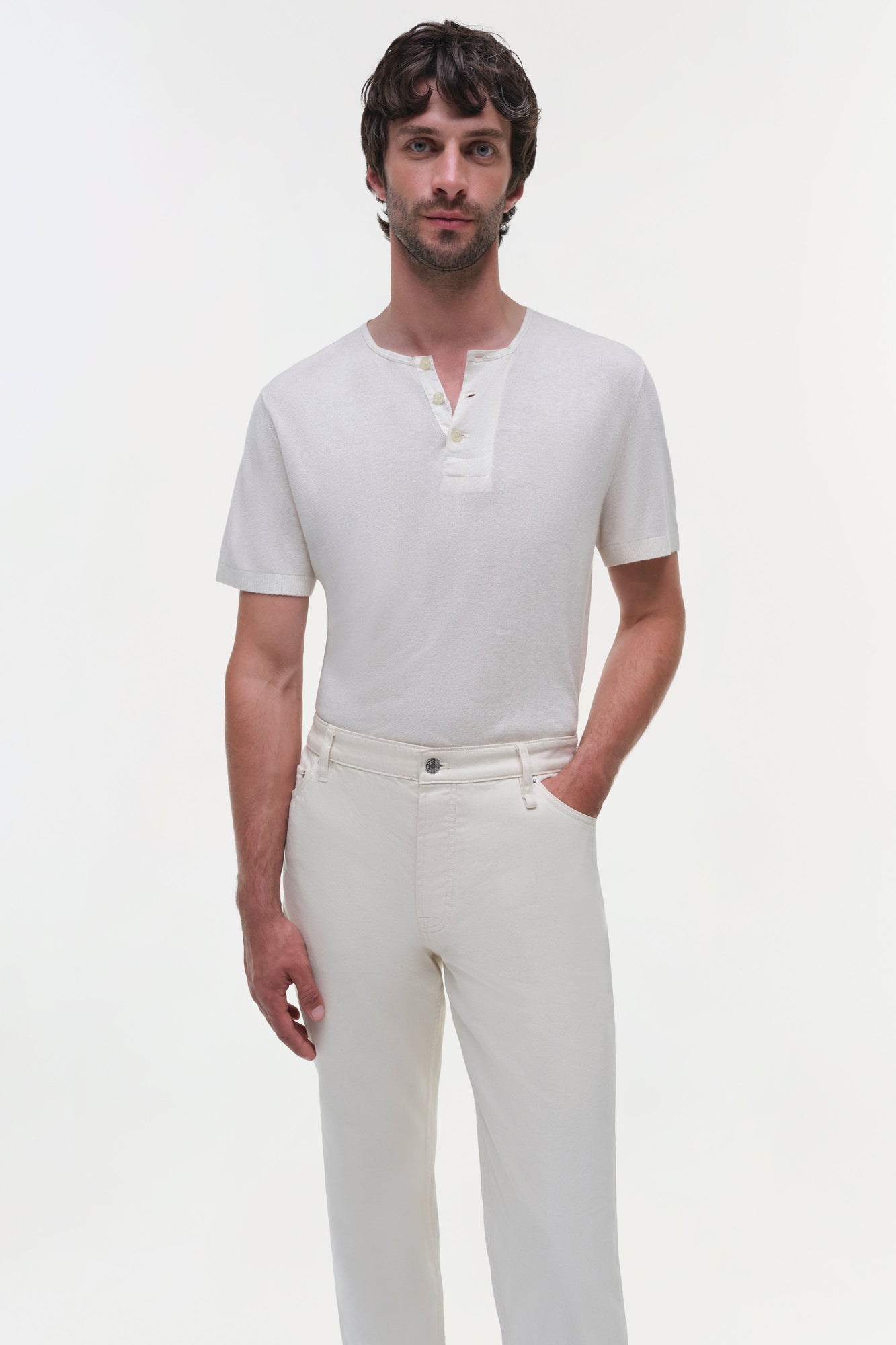Man wearing cream-colored wide leg jeans with a white short-sleeve henley shirt.