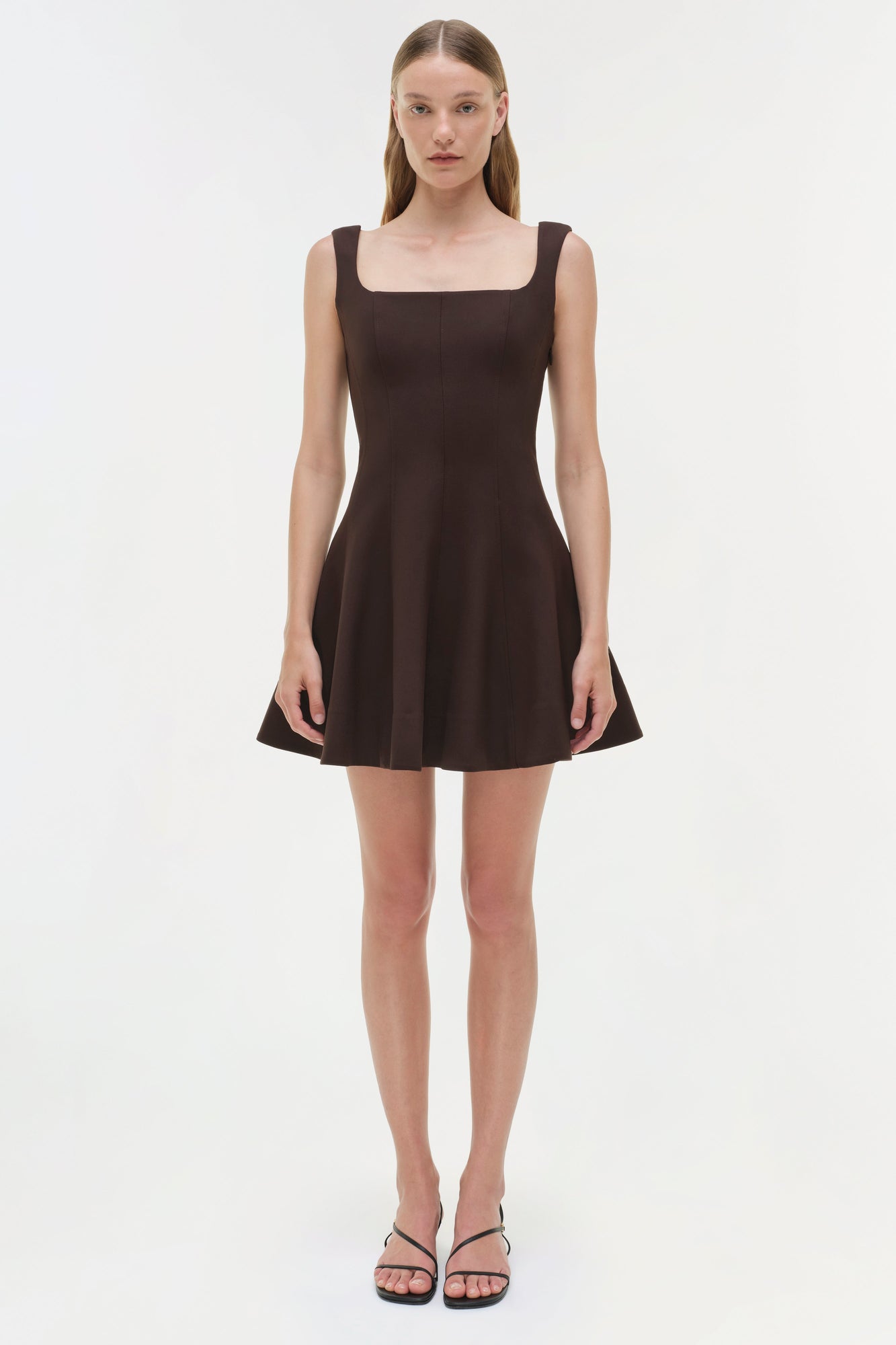 Black sleeveless mini dress with square neckline and fitted bodice, worn with black strappy sandals.