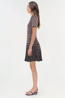 Woman wearing a dark navy knit mini dress with white wavy stripe pattern and short sleeves, shown in side profile view.