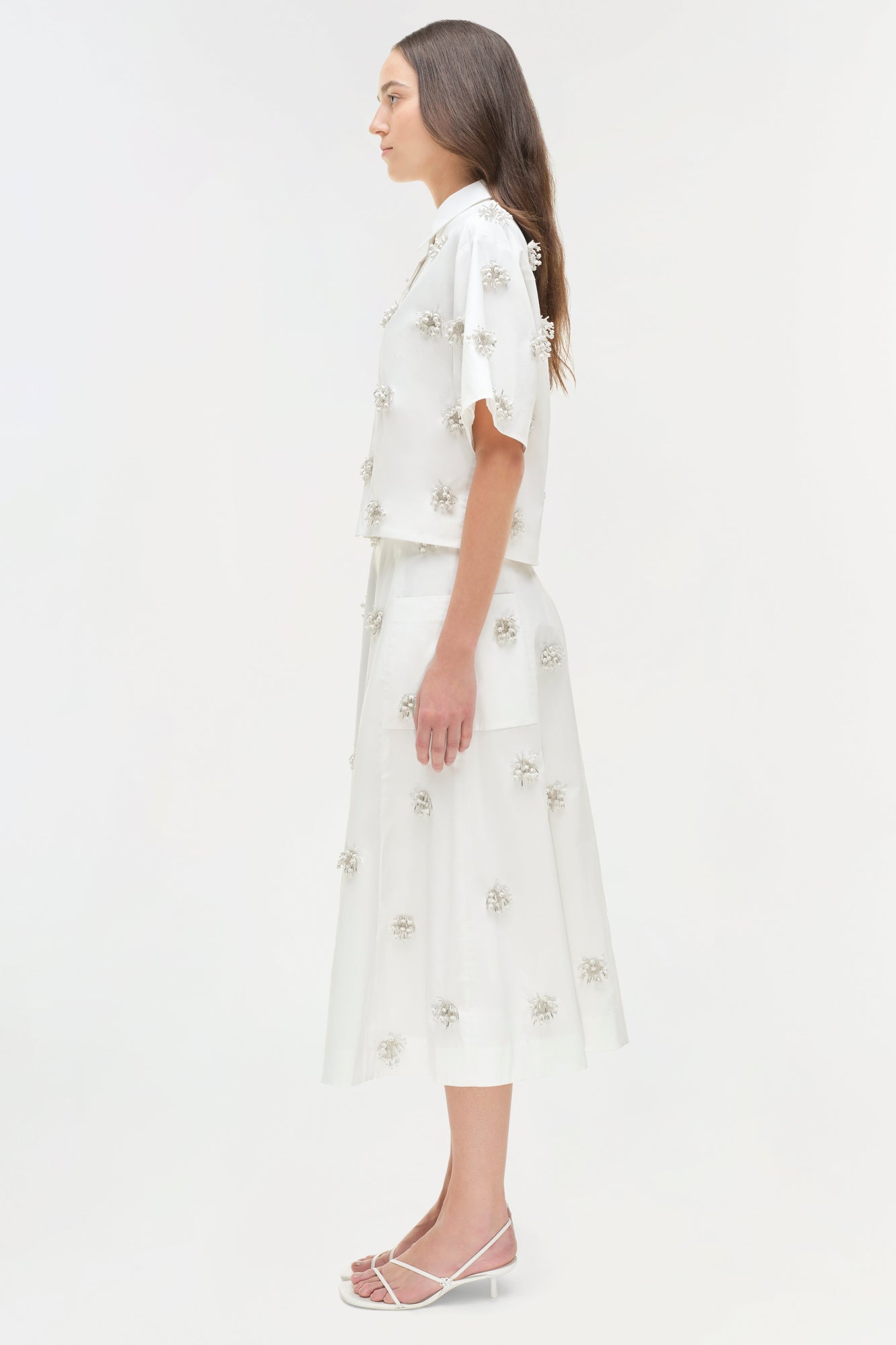 White camp shirt and midi skirt set with silver beaded embellishments throughout, shown on model in side profile.
