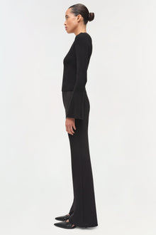 Woman wearing black wool long-sleeve top with wide-leg trousers, shown in side profile.