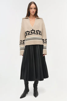 Beige V-neck sweater with black geometric and geometric patterns worn with black pleated skirt and boots.