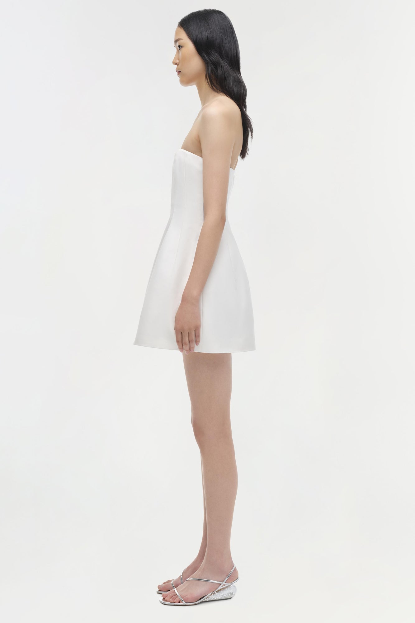 White strapless mini dress with an A-line silhouette, shown on model in side profile view.