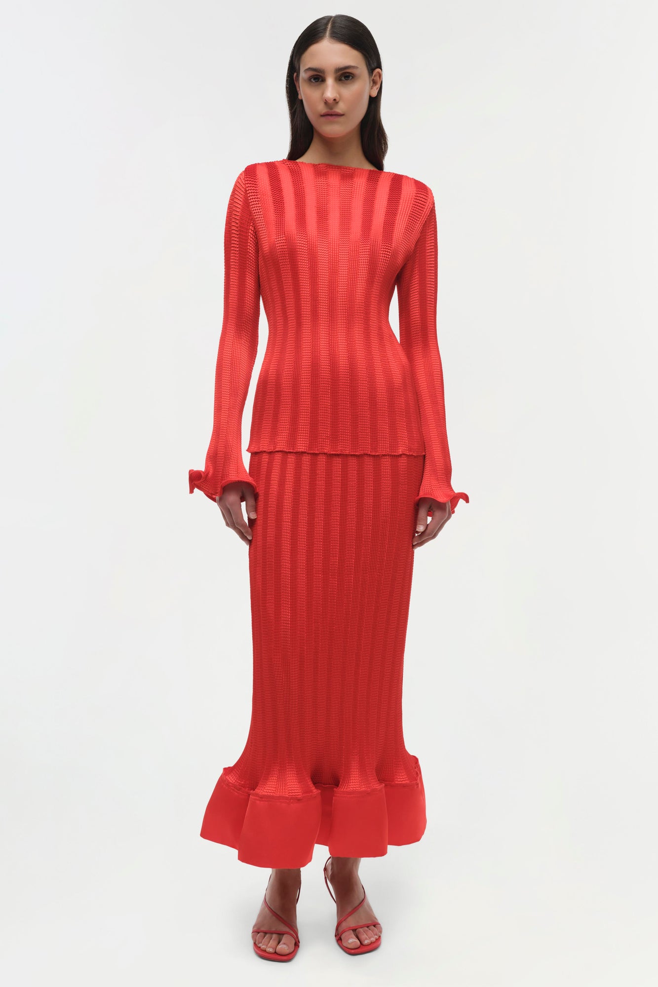 Woman wearing red ribbed long-sleeve top with ruched cuffs and matching midi skirt with ruffled hem.