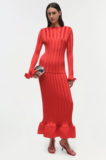 Woman wearing a red ribbed long-sleeve top with ruffled cuffs and matching maxi skirt with ruffle hem.