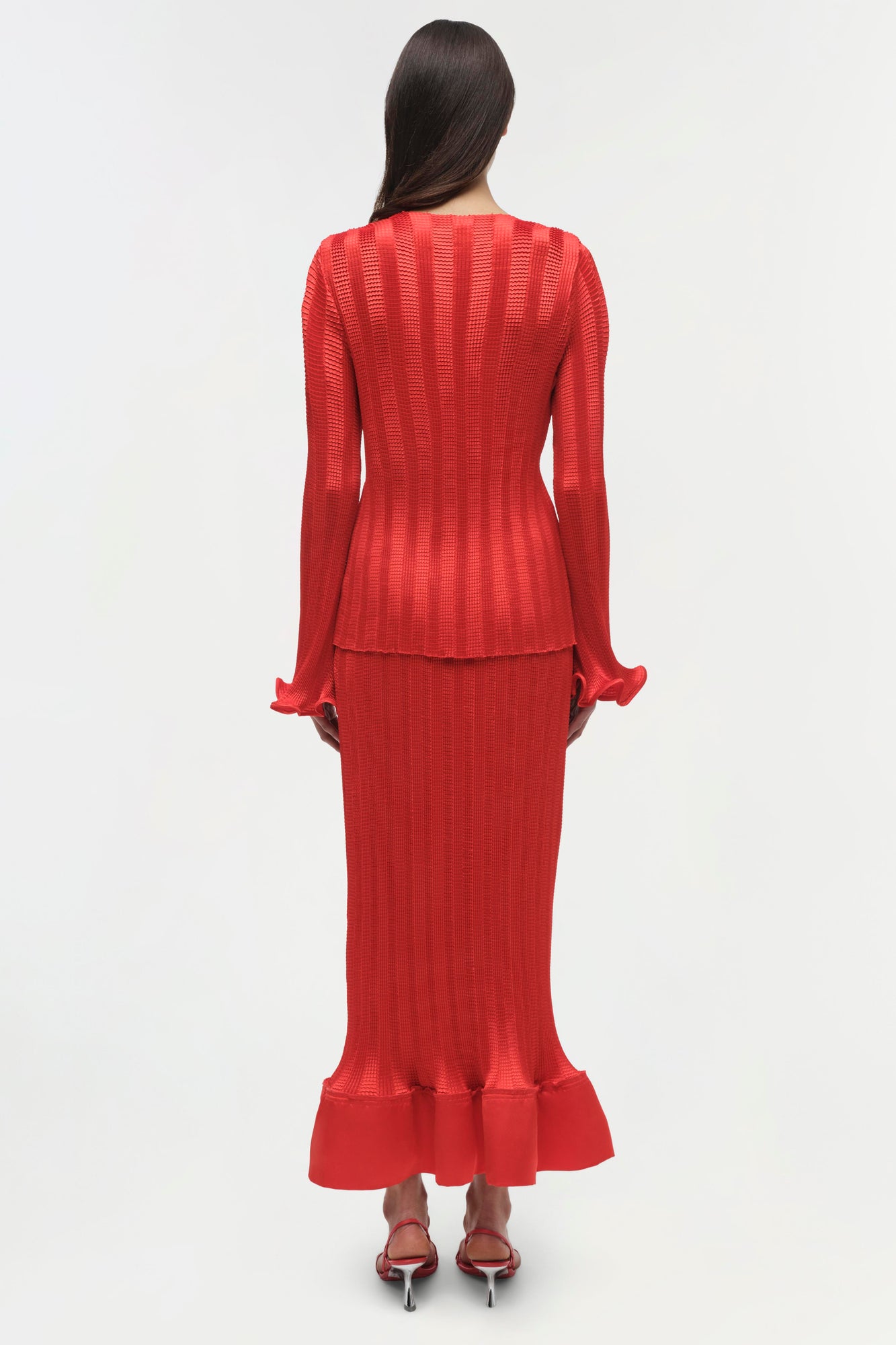 Red ribbed knit top with long sleeves, ruched cuffs, and fitted silhouette worn with matching midi skirt.