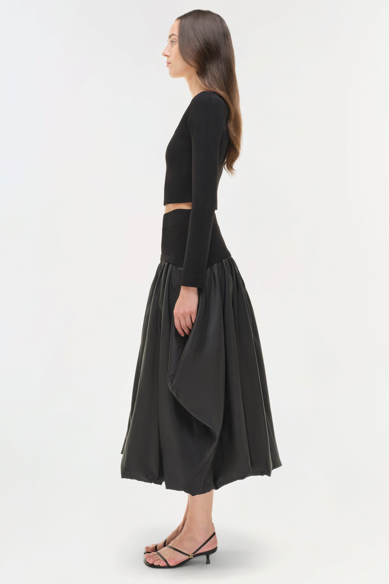 Black cropped knit long-sleeve top with cutout at waist, styled with voluminous mid-calf skirt.