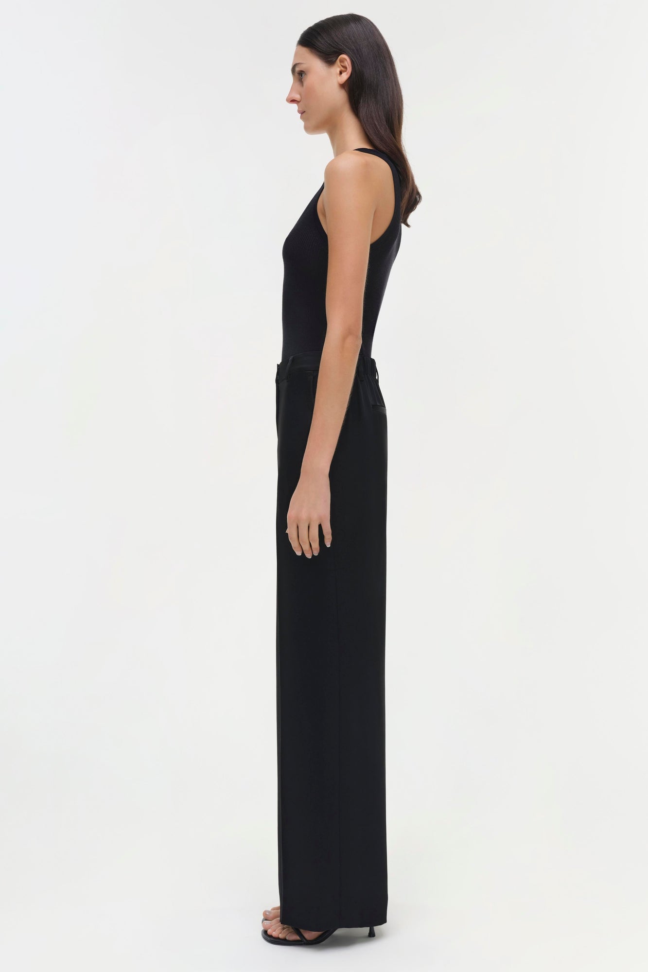 Black sleeveless pants with high waist and wide legs shown on model in side profile.