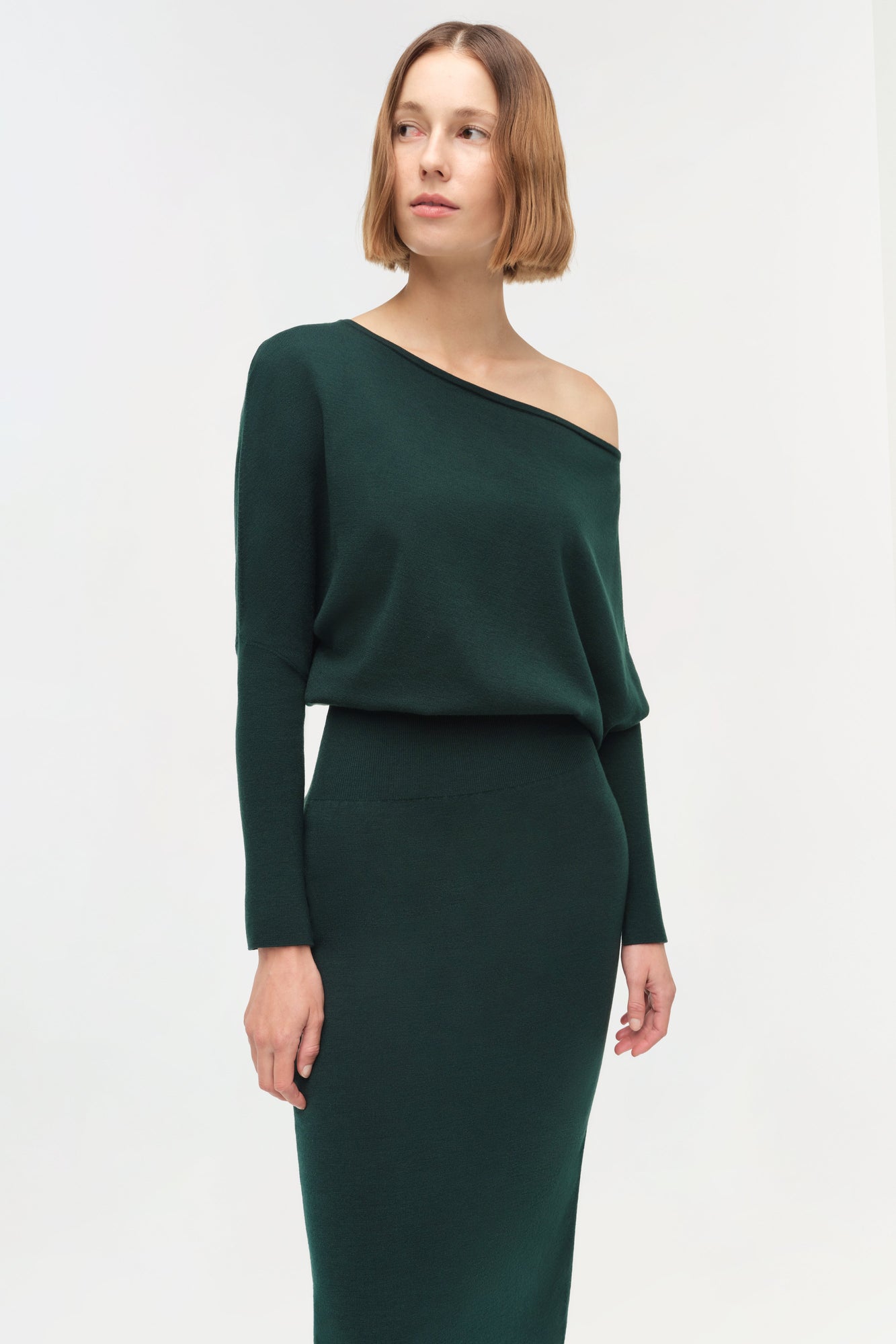 Woman wearing dark green off-shoulder midi dress with long sleeves and fitted skirt.