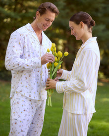A man with short gray hair wears the Men's Twill Pajama Set in Easter Frolic—white pants and a long-sleeve top with a small, colorful print—standing barefoot against a plain light background.