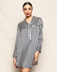 A woman stands against a light beige background, looking at the camera with her hair tied back and bold red lipstick, wearing the Petite Plume Womens Silk Nightshirt in Black and White Bengal Stripe.