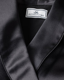 Close-up of a Womens Silk Short Robe in Black by Petite Plume, showcasing its luxurious hypoallergenic Mulberry Silk with a smooth, glossy texture ideal for sleepwear.