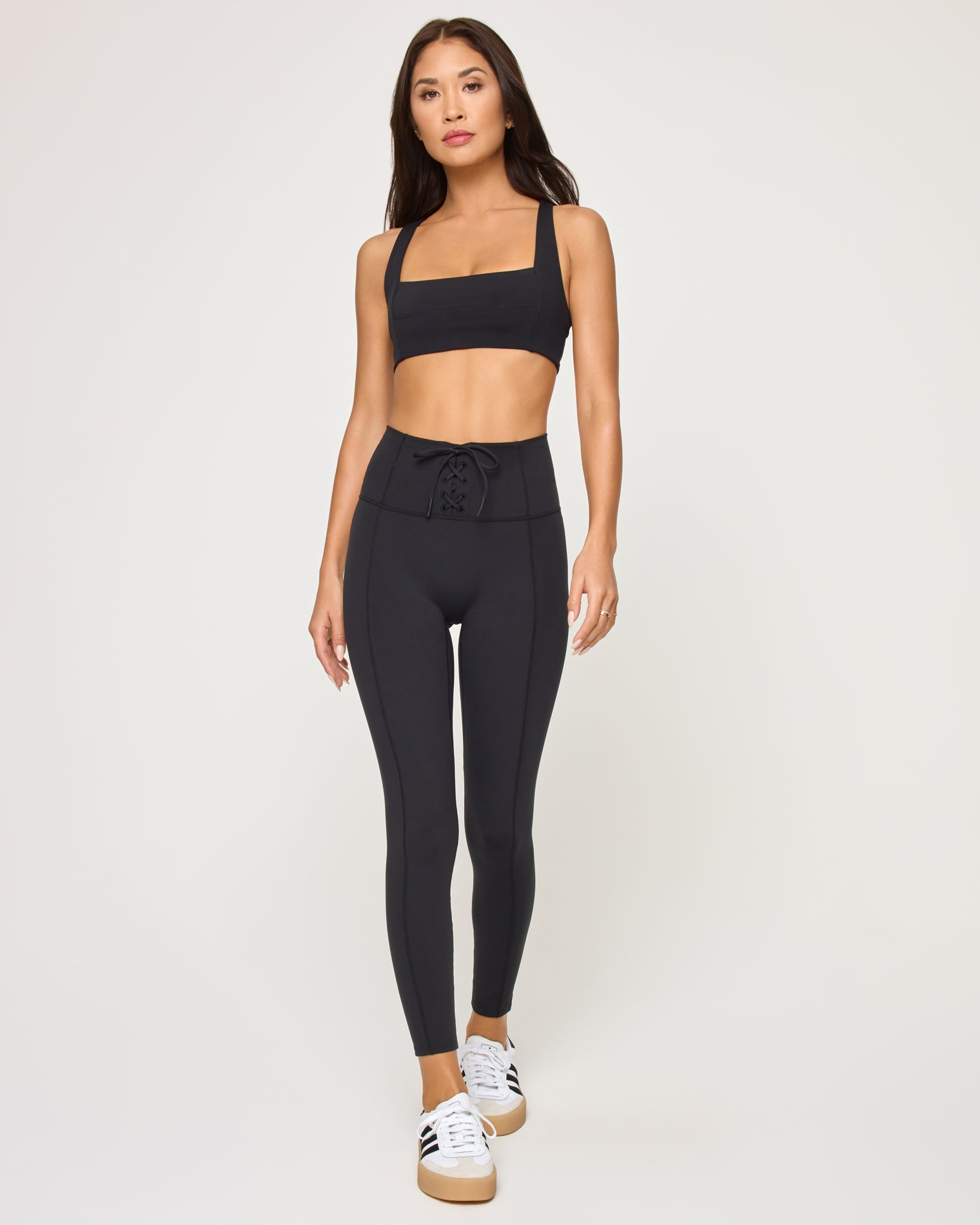 Front view of model wearing the Contender Legging in black, a high-waist legging with seam detail, with matching black sports bra and white sneakers.