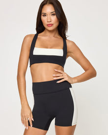 Close-up front view from the knees up of the LSPACE Uppercut Bra in black-cream on a model, showing the square neckline with cream trim detail paired with matching black-cream high-rise shorts.