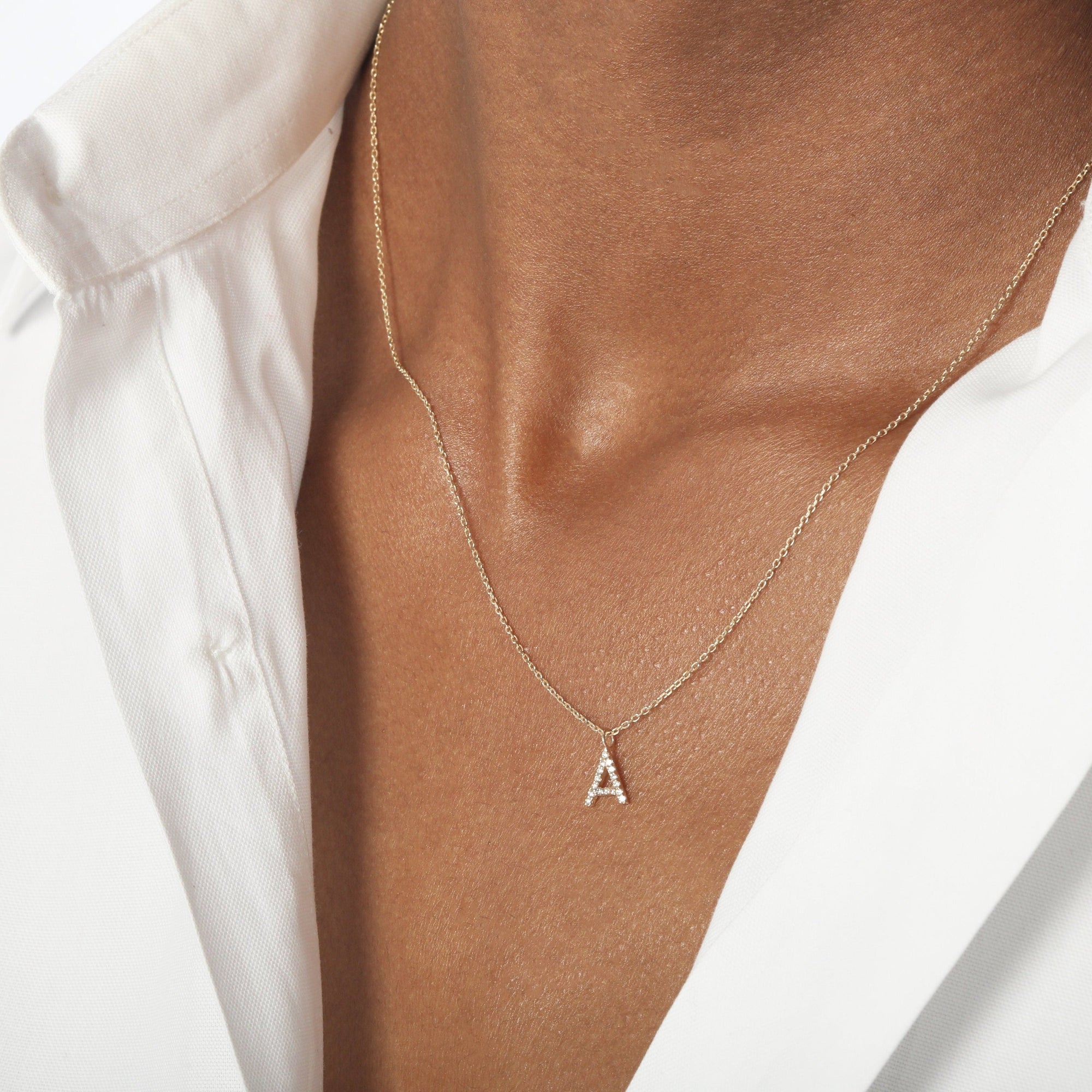 Model. Gold necklace with a 'A' pendant on a person wearing a white shirt.