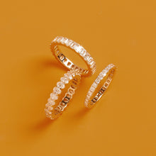 Flatlay Model Three gold diamond eternity rings resting together on a solid orange background
