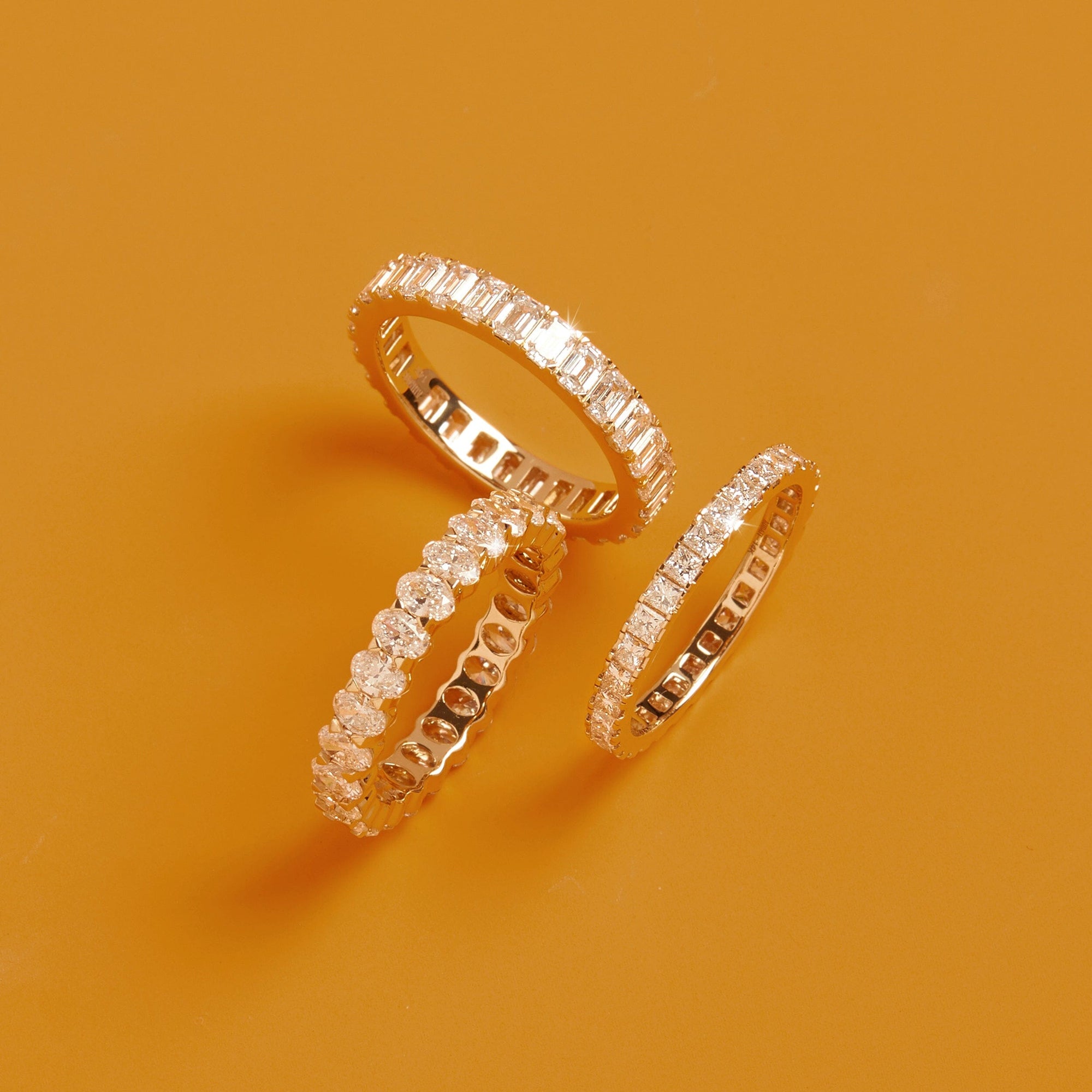 Flatlay Model Three gold diamond eternity rings resting together on a solid orange background