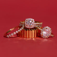Flatlay Model Close-up of four gold and diamond rings arranged against a deep red background. The collection features a delicate single-row diamond band, a thick ribbed gold band, a cushion-cut halo diamond ring, and an oval-cut halo diamond ring.