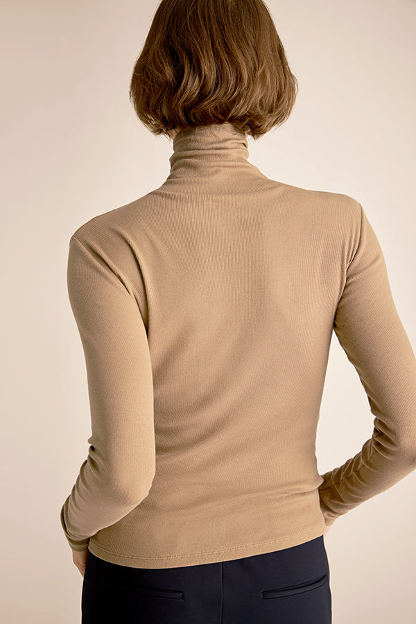 Woman wearing a beige turtleneck sweater against a beige background | Exclude | Grid Hover