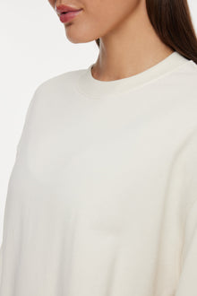 Model wears a white crewneck sweatshirt with logo on back that reads 