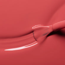 A close-up of a brush spreading glossy pink nail polish, creating smooth, fluid lines and a reflective surface.