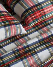 Close-up of a bed adorned with Petite Plumes Flannel Sheets in Balmoral Tartan, showcasing plaid sheets and pillowcases accented with red, green, blue, and yellow stripes on white. The cozy cotton brushed flannel creates a warm and inviting atmosphere.