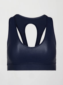 Model wears a navy, glossy, deep scoop-neck sports bra with a sleek racerback and a shiny, liquid-like finish.
