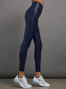 Model is wearing navy high waisted performance leggings in a liquidy-shine finish that hit at the ankle.