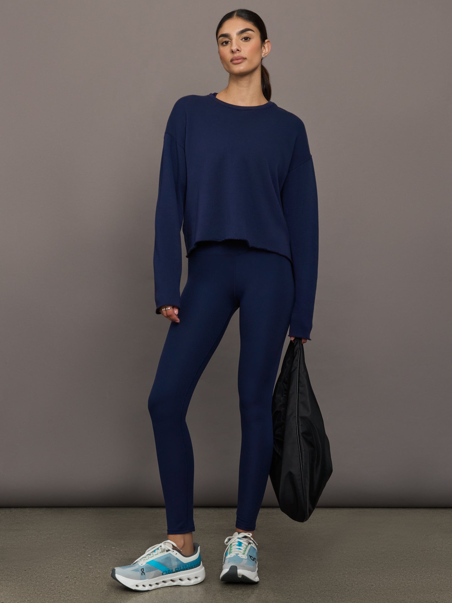 Woman wearing a navy blue outfit holding a black bag against a gray background