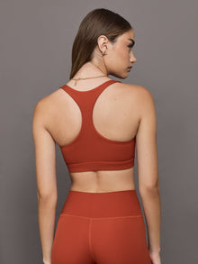 Model wears terracotta-colored racerback bra with a ribbed texture, square neckline, and wide straps that merge at the back.
