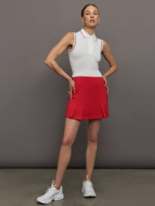 Model wears a sleeveless white tennis polo with three buttons and red seam detailing. 