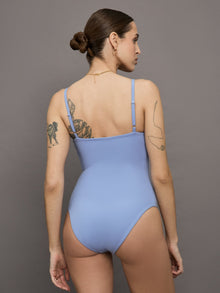 Model wears a periwinkle colored body suit with a straight neckline across the chest and thin straps. 