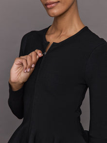 Model wears black long-sleeve zip-up sweater with a fitted bodice and flared peplum hem.