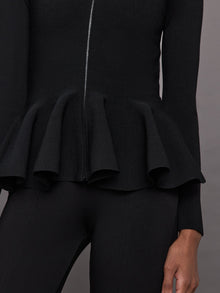 Model wears black long-sleeve zip-up sweater with a fitted bodice and flared peplum hem.