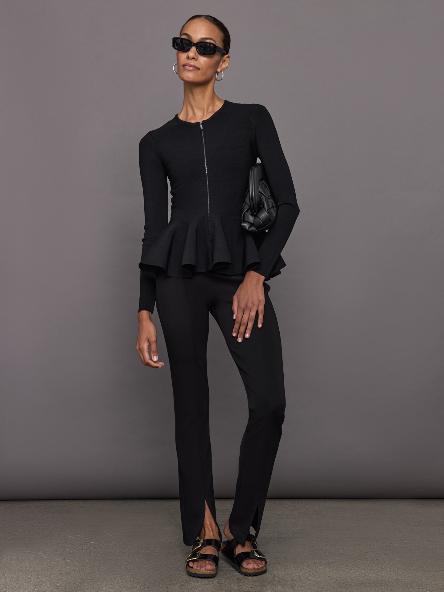 Model wears black long-sleeve zip-up sweater with a fitted bodice and flared peplum hem.