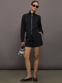 Model wears black Interlock Full Zip Jacket featuring a sleek, minimalist design with a high collar and full-length zipper.