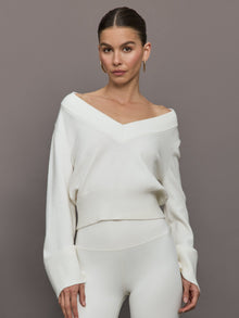 Model wears a white v neck bell sleeved sweater. 