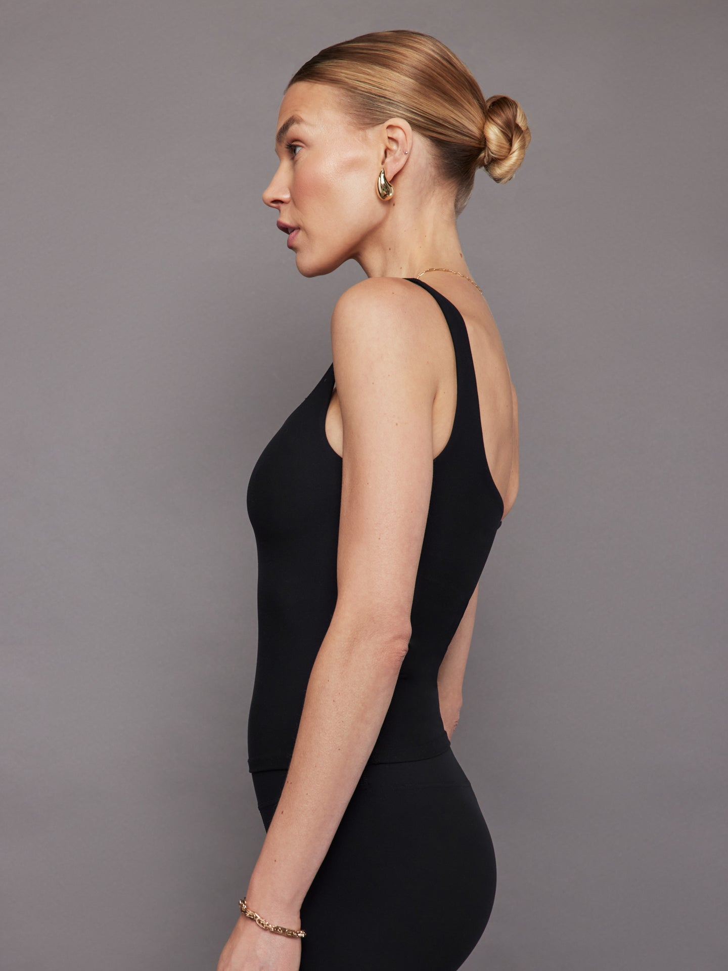 Model wears a black, fitted tank top with a wide scoop neckline and a smooth, soft-looking finish.
