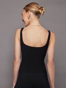 Model wears a black, fitted tank top with a wide scoop neckline and a smooth, soft-looking finish.
