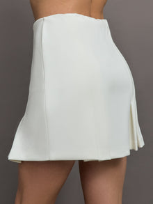 Model wears a white pleated miniskirt. 