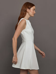 Model wears a white sleeveless tennis dress with pleating below the waist.