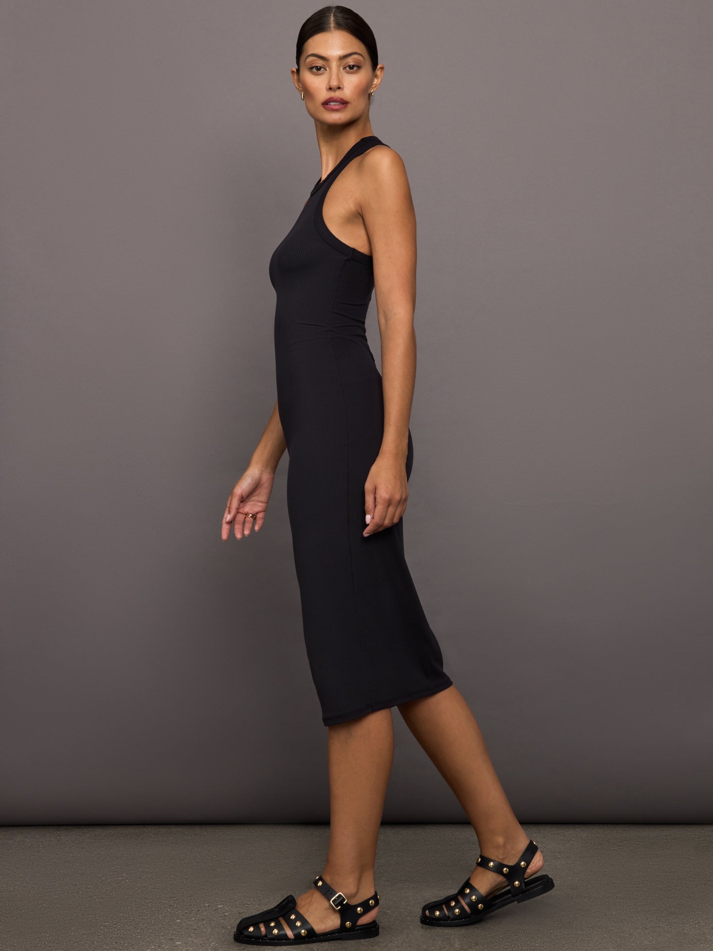 Woman wearing a black ribbed sleeveless dress against a gray background